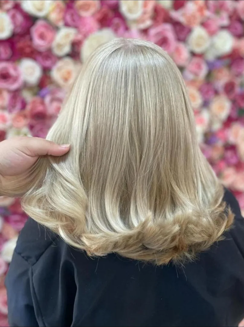 Cabelo loiro claro na altura dos ombros, liso com pontas viradas, visto de costas diante de um painel de rosas