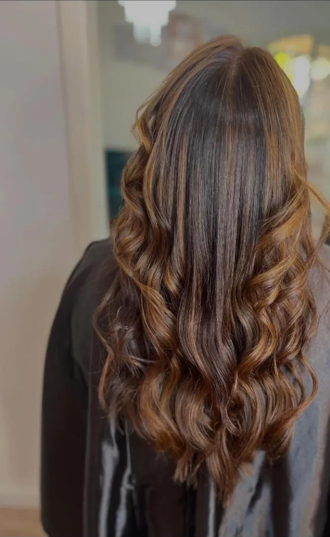 Cabelo castanho com mechas acobreadas e cachos largos, visto de costas